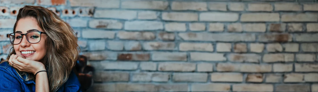 A woman smiling in front of a brick wall.