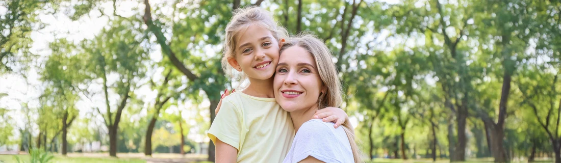 A mom and daughter smiling in a park.