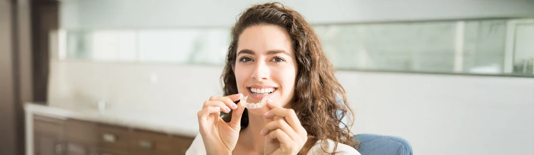 A woman holding a Invisalign up to her teeth.