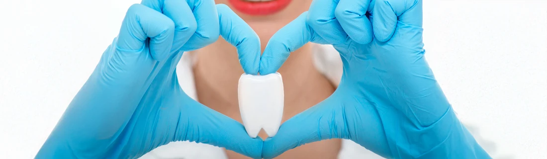 A person making a heart shape with their hands. There is a fake tooth in the center.